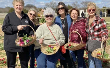 6 women taking a group photo holding baskets of fresh food after a service project